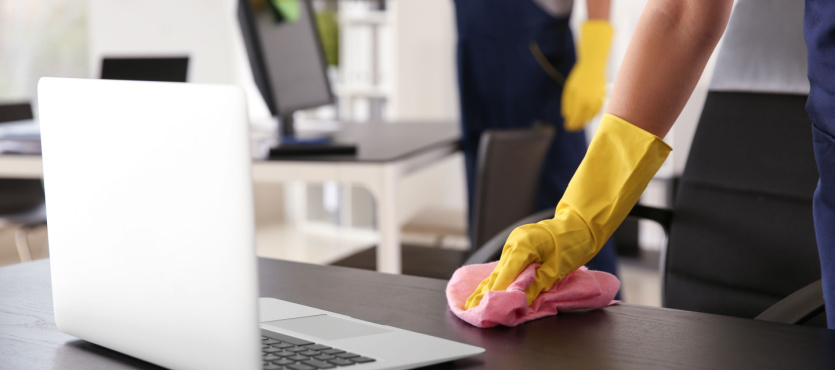 Gloved hand wiping a desk beside a laptop for an office cleaning company in Plantation