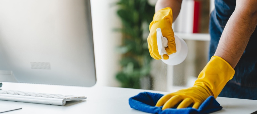 Gloved hand wiping a desk near a computer during commercial cleaning in Pompano Beach