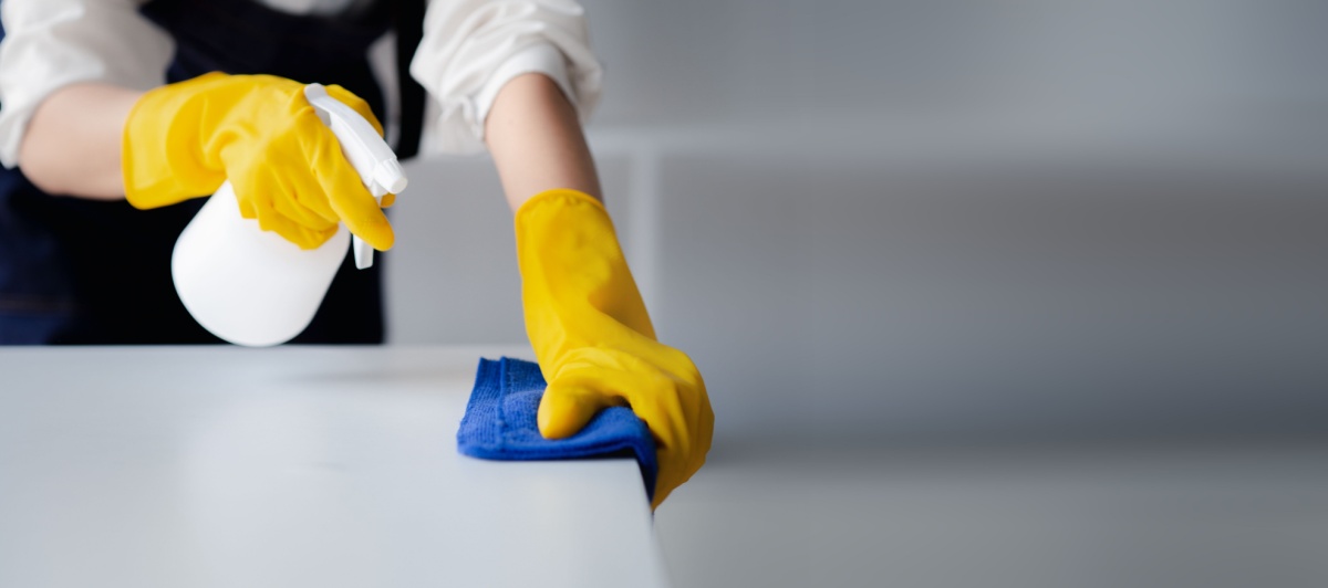 Gloved hand spraying and wiping a desk during commercial cleaning in Coral Springs