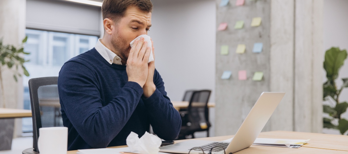 Man sneezing at his desk from allergens that janitorial services in Pompano Beach help reduce