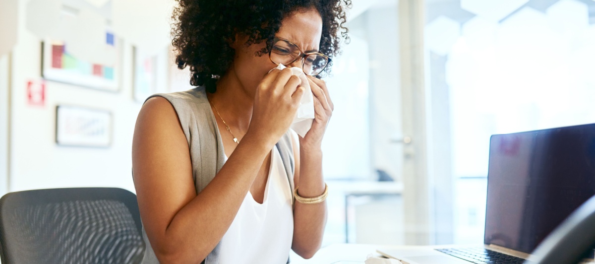 Office worker sneezing at her desk during flu season, helped by janitorial services in Coral Springs