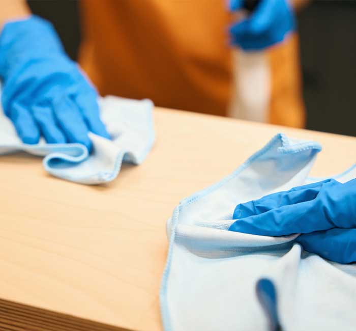 Blue-gloved hands wiping a desk during janitorial services in Delray Beach